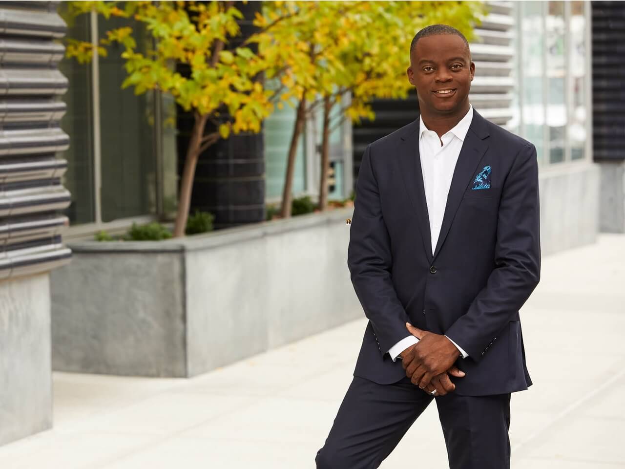 Photo of Charlie Lewis, HUAA President, standing up in black suit with planters in background