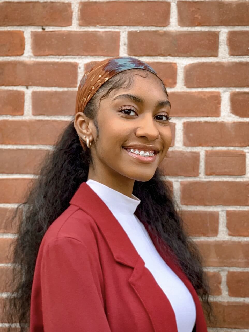 Cienna Benn headshot against brick wall wearing red suit