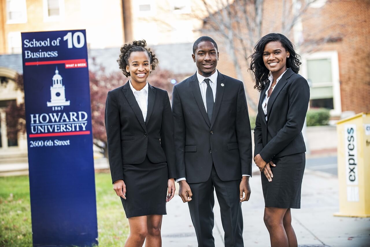 Three Howard School of Business students pose by sign