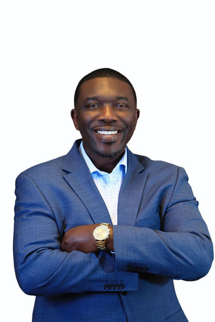 Shawn Joseph in blue suit arms folded against white background 