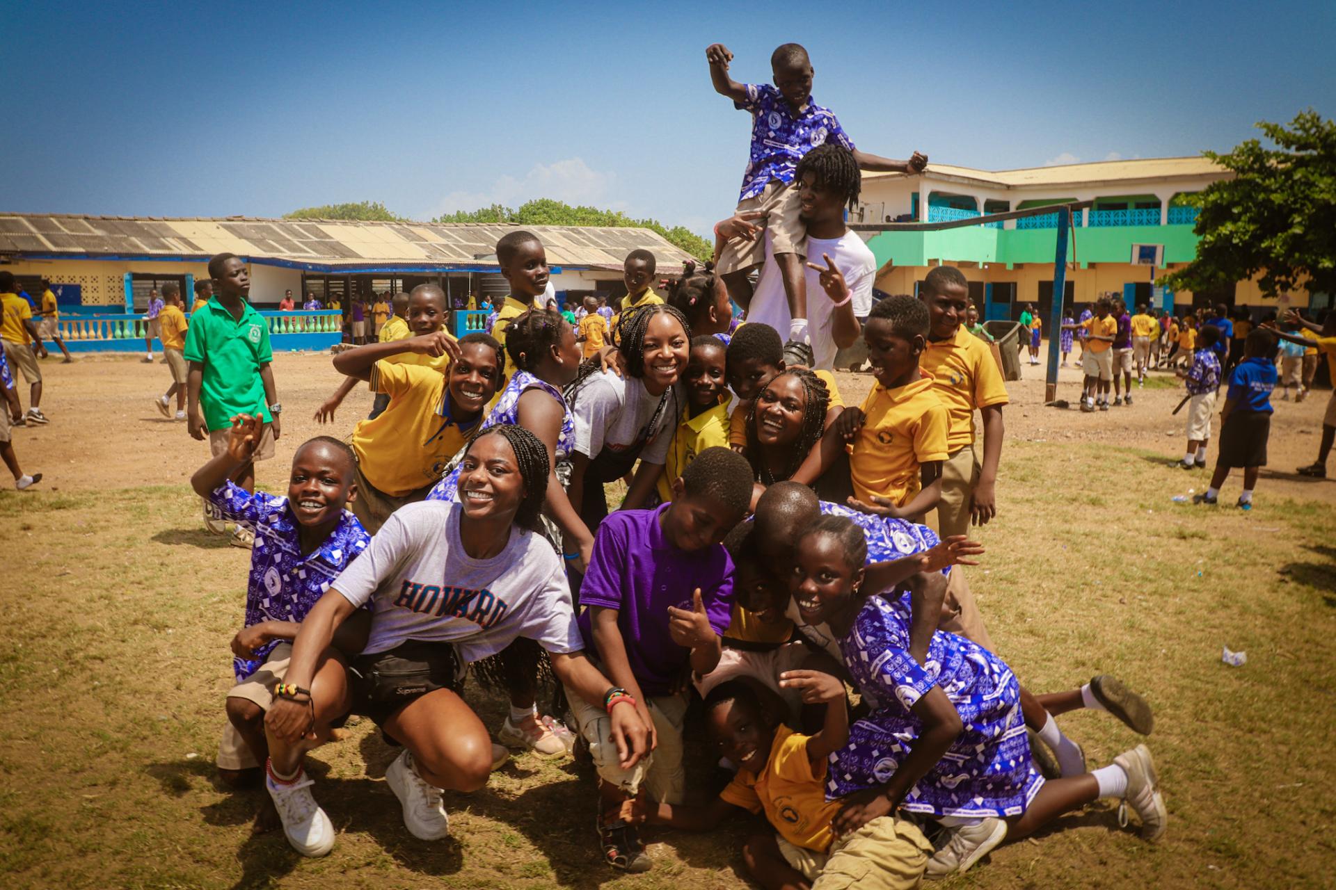 During their recess times, students of Kwame Nkrumah Memorial School hug and jump all over Howard Students as they pose. Students in the image include (from left to right): sophomore Veronika Victor, senior Tori Miller; junior Miah Powell, senior Eric January