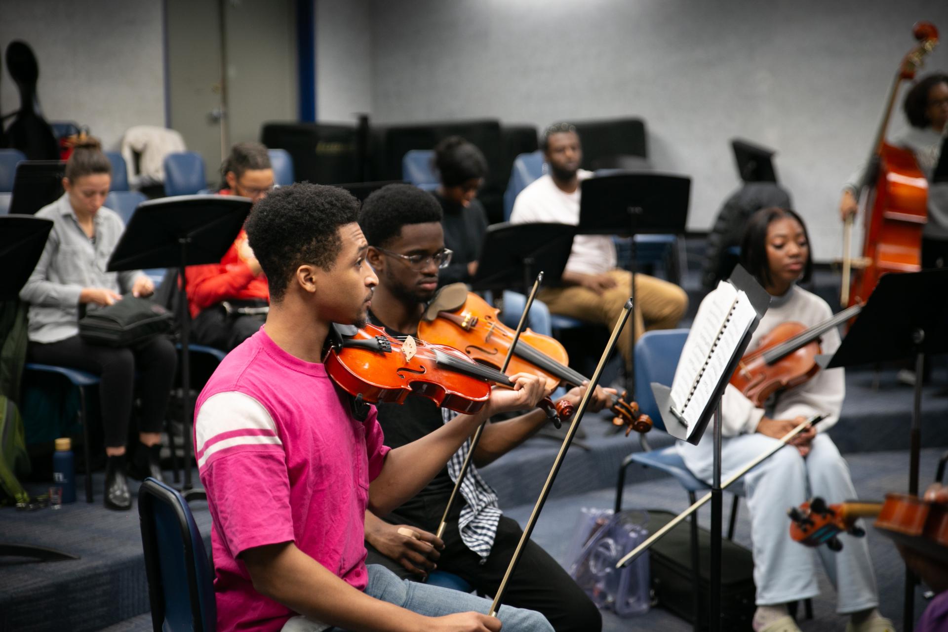 Student members of the HU Orchestra’s string section hold their instruments in resting positions while receiving further instruction from the conductor. 