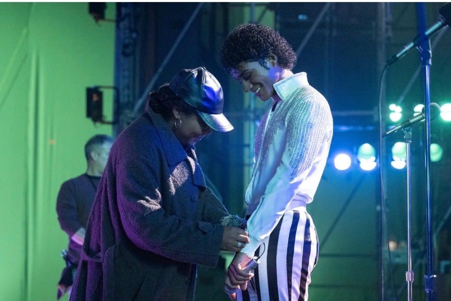 Two people on a movie set. The woman on the left, the costume designer, is fixing the garments of the man on the left who is smiling