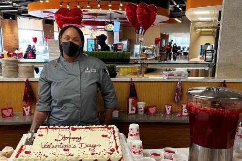 Chef standing by sheet cake that says Happy Valentine's Day