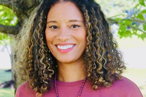 Black woman with curly hair standing in front of a tree
