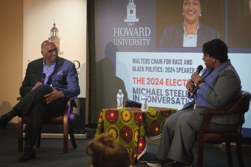 Stacy Abrams and Michael Steele holding microphones on a stage in Howard University's School of Business as they discuss the 2024 election