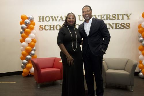 Two people standing side by side in front of a sign that says Howard University School of Business. There is a multi ballon structure in different colors on the right and left side of the image