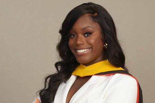 Woman in a white suit that has her arms folded. she has a phd regalia across her neck. 