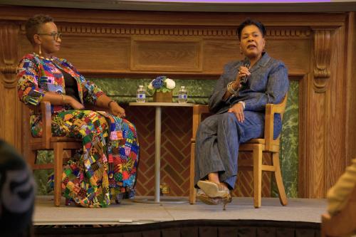 Two women sitting on a stage with microphones in their hands. There is a small table in between them with two small water bottles on top