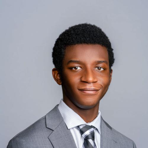 Logan Ross wearing a gray suit, white shirt and blue and white tie.