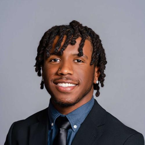 Maize Booker wearing a black suit with a blue button down and black tie