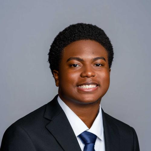 Joshua Clemons wearing a black suit jacket with a white button down shirt and royal blue tie