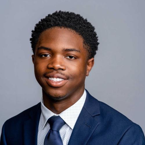 Jonathan Greer wearing a dark blue suit jacket with a white and blue polka dot button down and a dark blue tie