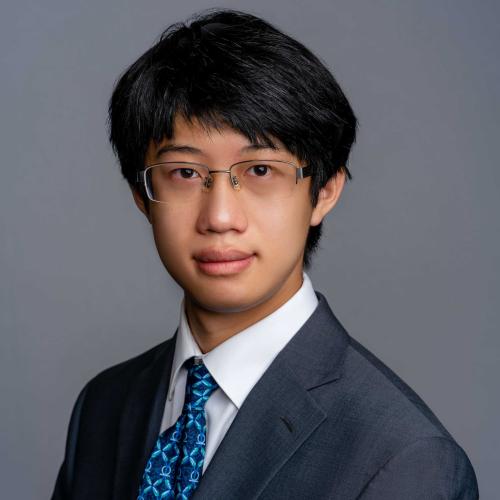 James Hsia wearing a dark grey suit jacket with a white button down shirt and a blue patterned tie