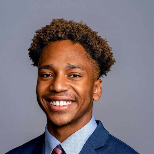 Jon-Edward Stokes wearing a blue suit jacket with a light blue patterned shirt and a multicolor striped tie