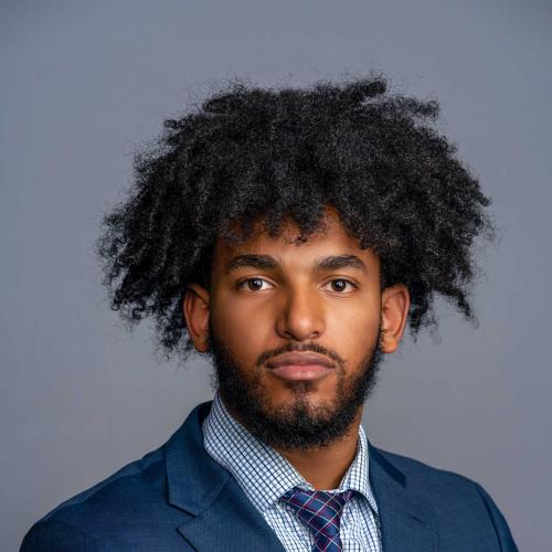 Selama Tesfamariam wearing a blue suit jacket with a blue and white patterned shirt and a blue, red, and white plaid tie