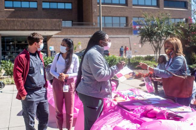 people receiving information at a pink table about breast cancer outside hospital