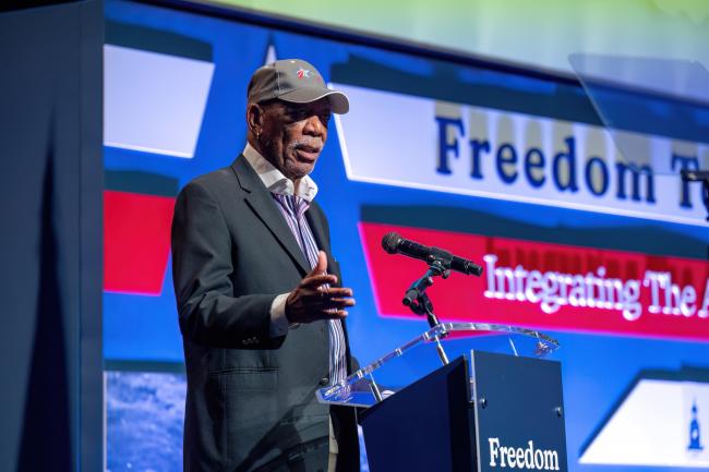 Morgan Freeman stands at a podium on stage in Cramton Auditorium