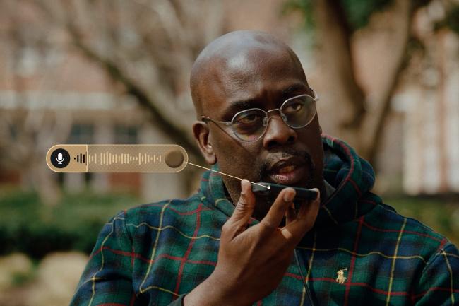 Black man with glasses speaks into his iPhone on the Howard University Yard