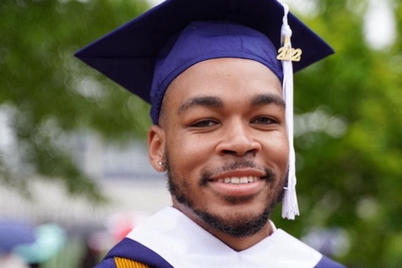 Young Black Howard grad Colin Joseph stands dressed in purple graduation regalia