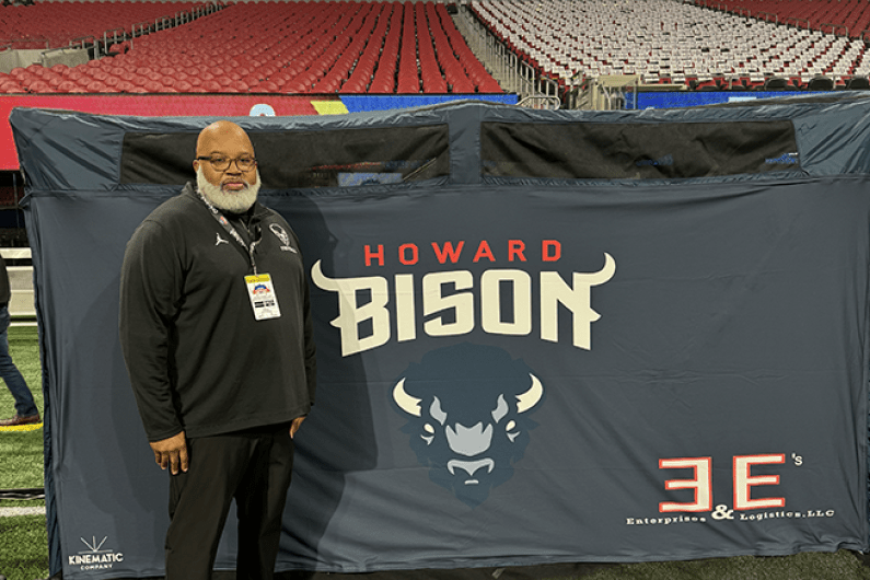 Eryk Marsh, men's football equipment manager, stands on football field in front of Bison banner