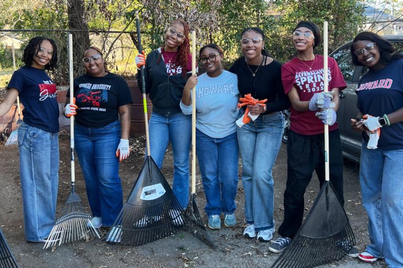 A group of seven howard students outside. Many of them are holding rakes. They are all wearing Howard-embossed sweatshirts and t-shirts. 