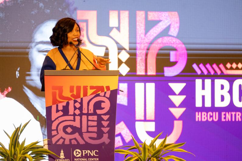 Black woman wearing orange stands at a podium at the PNC HBCU Empower conference