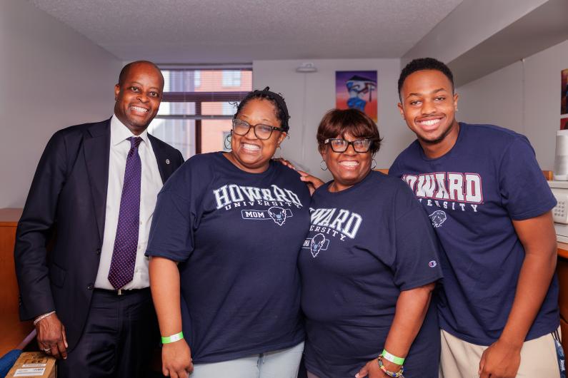 Howard University President Wayne Frederick wearing a suit and tie alongside three family members who are wearing Howard-branded t-shirts