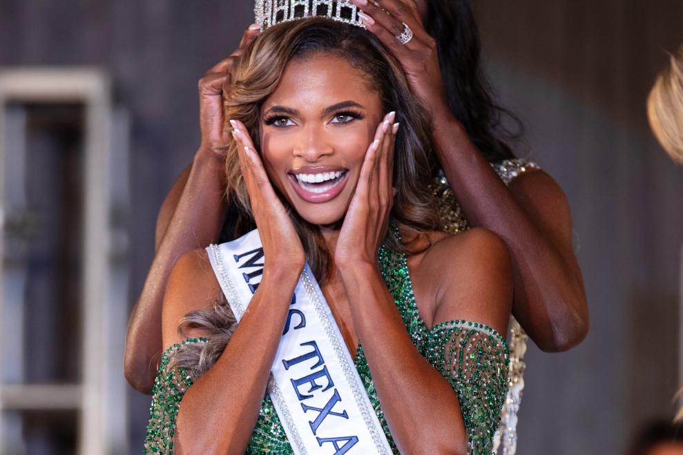 Woman being crowned at the Miss Texas USA 2025 competition. She is holding her face and smiling. She is wearing a sash and is being crowned