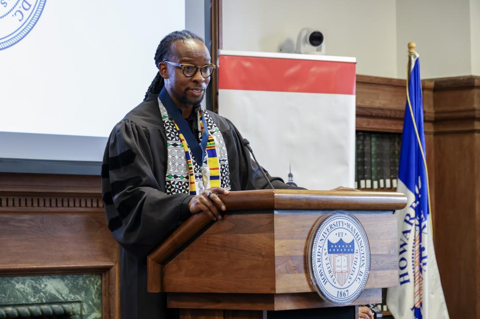 A man standing behind a wooden podium that has a slim black microphone attached.