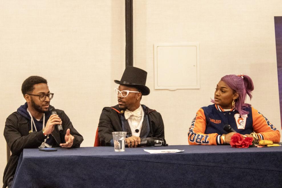 Alvin Hannon Blerdcon panelist. There are three people sitting behind a long table. Hannon is on the far left and he is holding a microphone