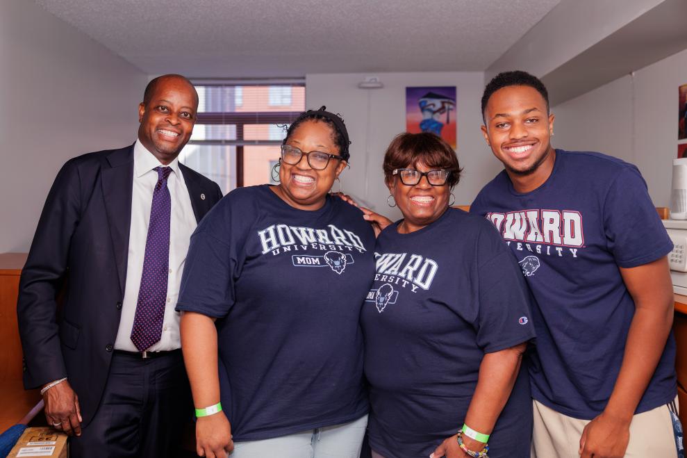 Howard University President Wayne Frederick wearing a suit and tie alongside three family members who are wearing Howard-branded t-shirts