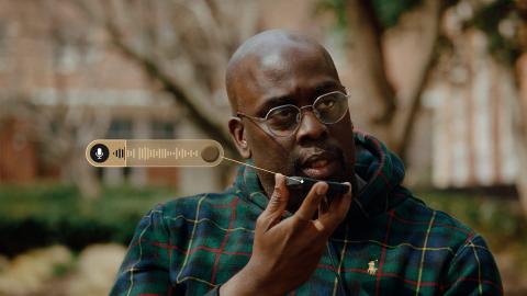 Black man with glasses speaks into his iPhone on the Howard University Yard
