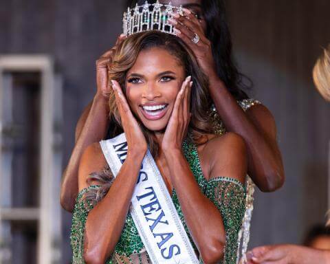 Woman being crowned at the Miss Texas USA 2025 competition. She is holding her face and smiling. She is wearing a sash and is being crowned