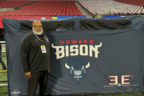 Eryk Marsh, men's football equipment manager, stands on football field in front of Bison banner