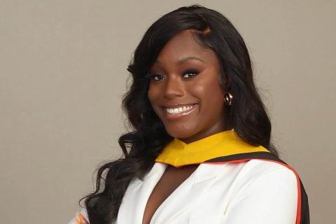 Woman in a white suit that has her arms folded. she has a phd regalia across her neck. 