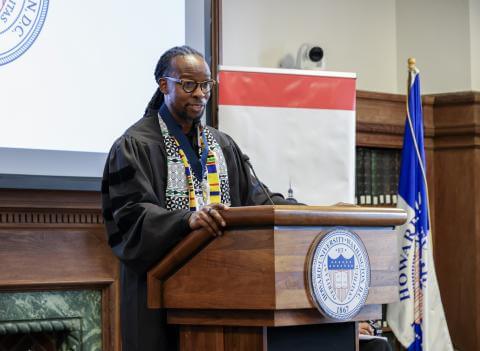 A man standing behind a wooden podium that has a slim black microphone attached.