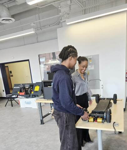Dean Kimberly Jones standing at a table with a male student as they look at a 3D printed mechanical skateboard made in the Howard University Makerspace