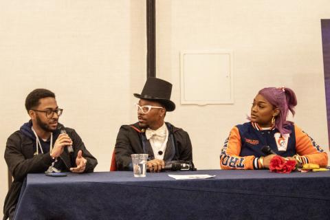 Alvin Hannon Blerdcon panelist. There are three people sitting behind a long table. Hannon is on the far left and he is holding a microphone
