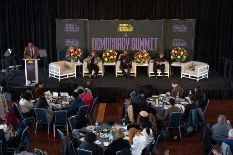 Three professionals sit on stage in front of a crowd at the Center for Journalism and Democracy Summit in 2024