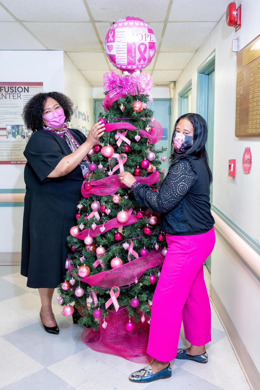 Two people decorate evergreen with pink decor for breast cancer awareness month