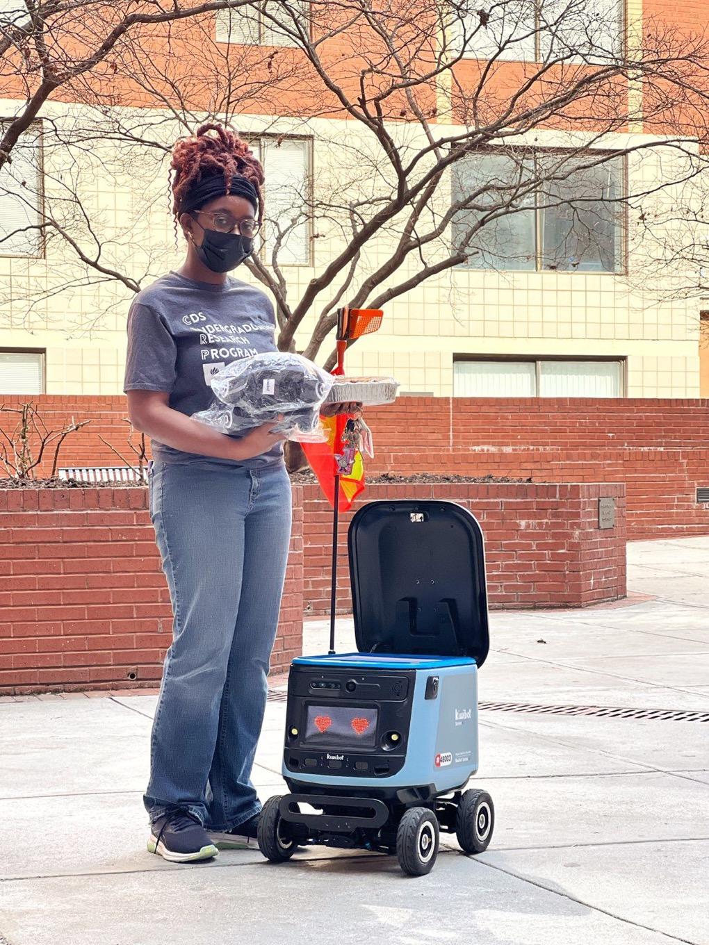 A student stands with a kiwibot
