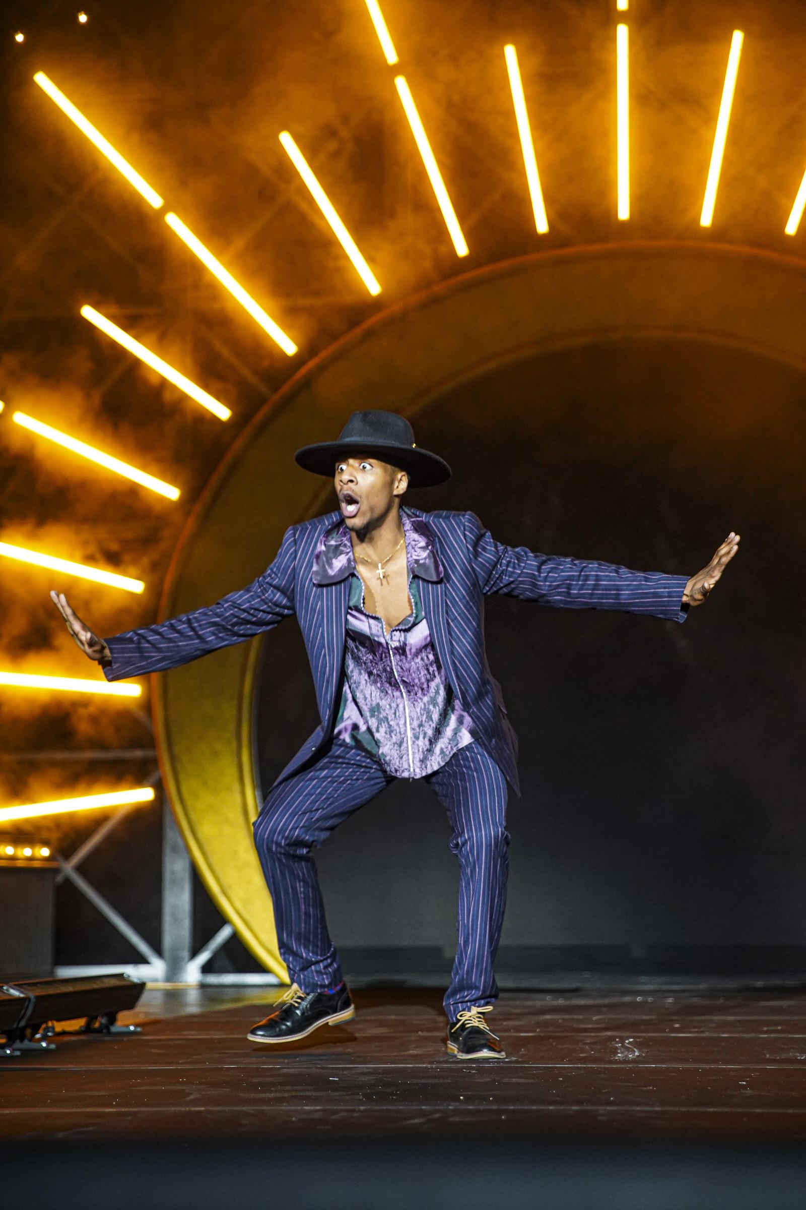 Fashion show host performs on stage with yellow lights behind him