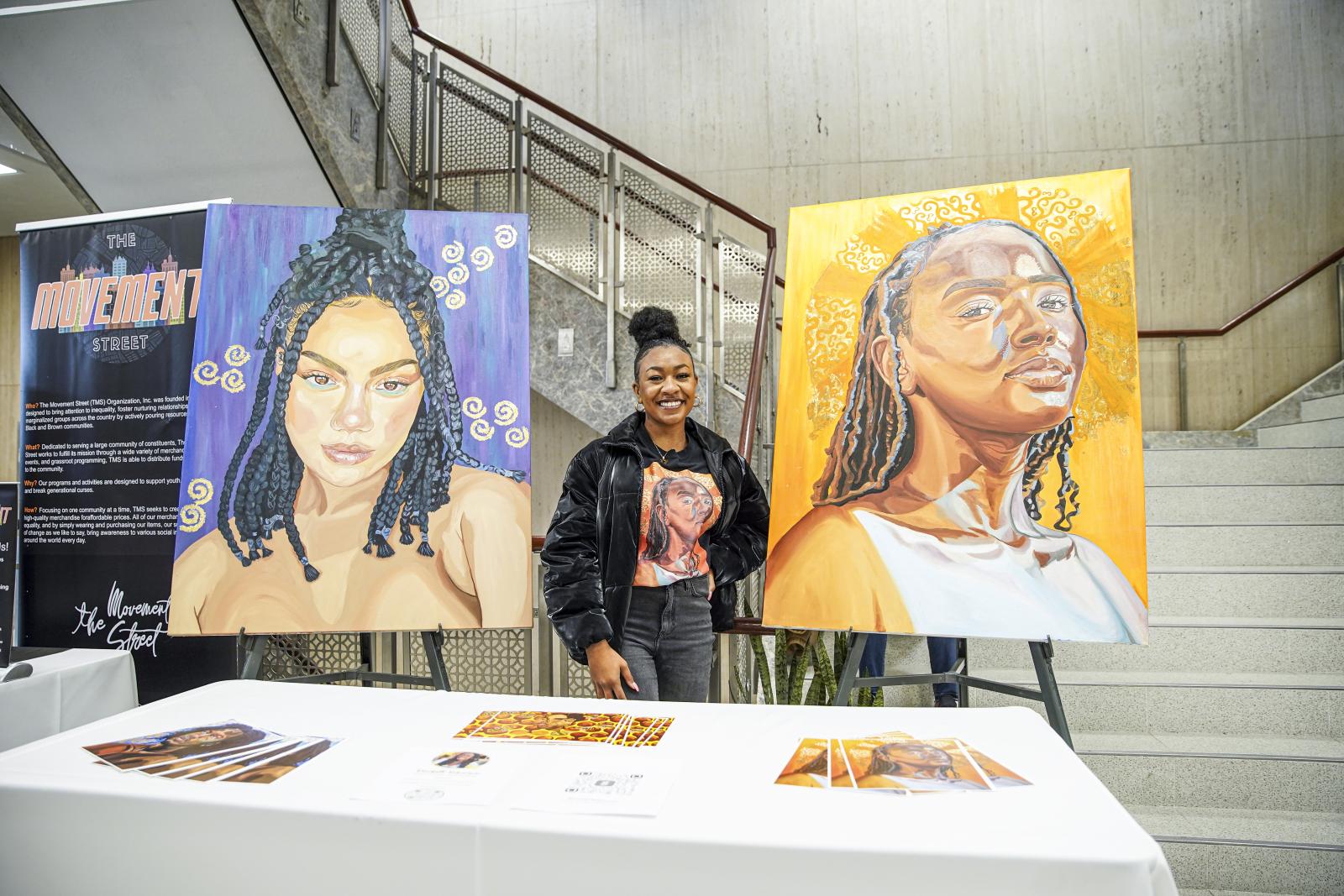 Student artist stands next to paintings