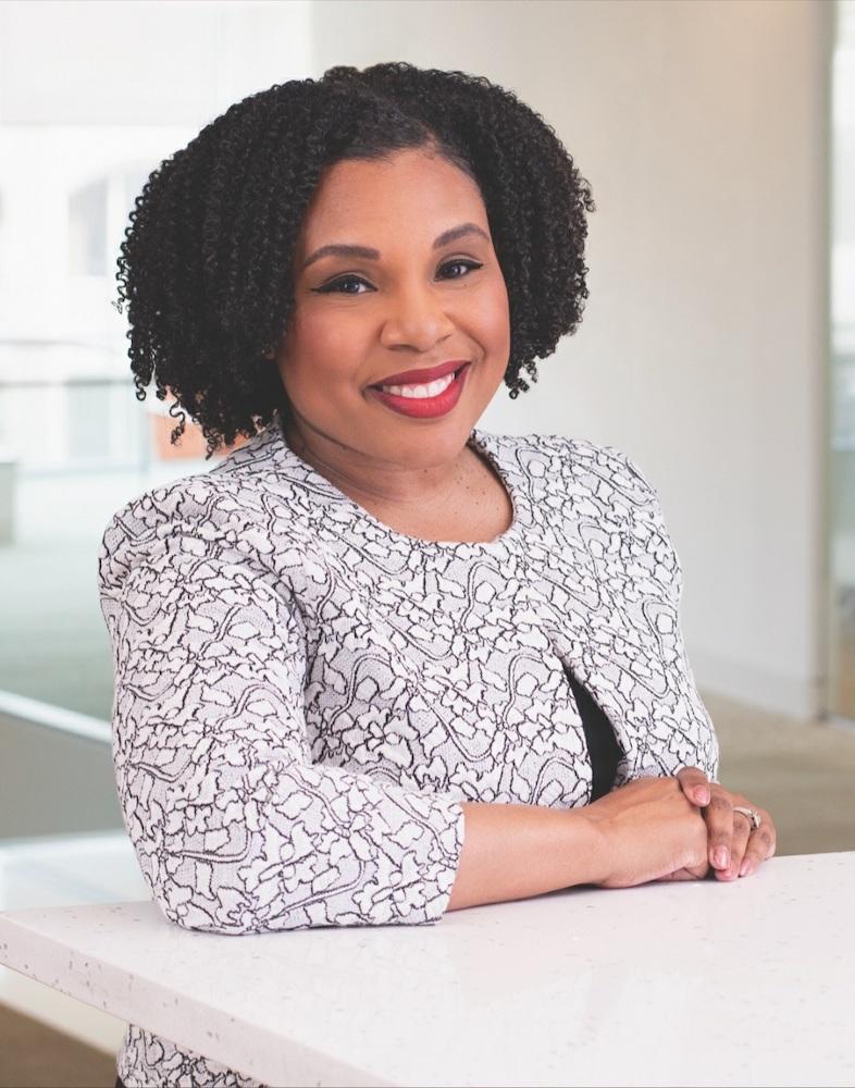 Professor Tiffany Wright with curly black hair poses in white blouse for headshot