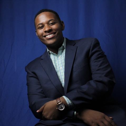 Black student poses with arms crossed against a dark blue background