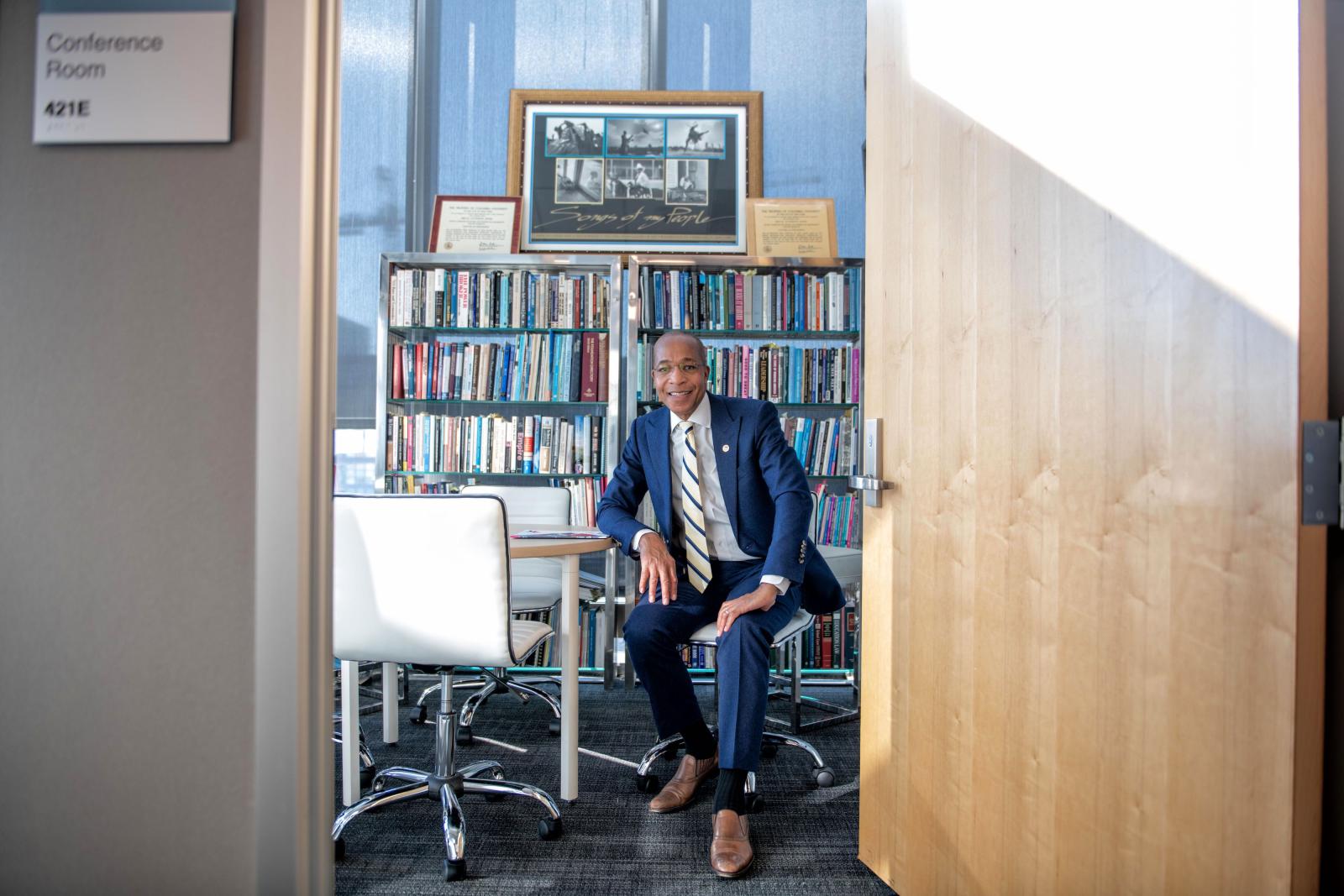 man in suit sitting in conference room with books