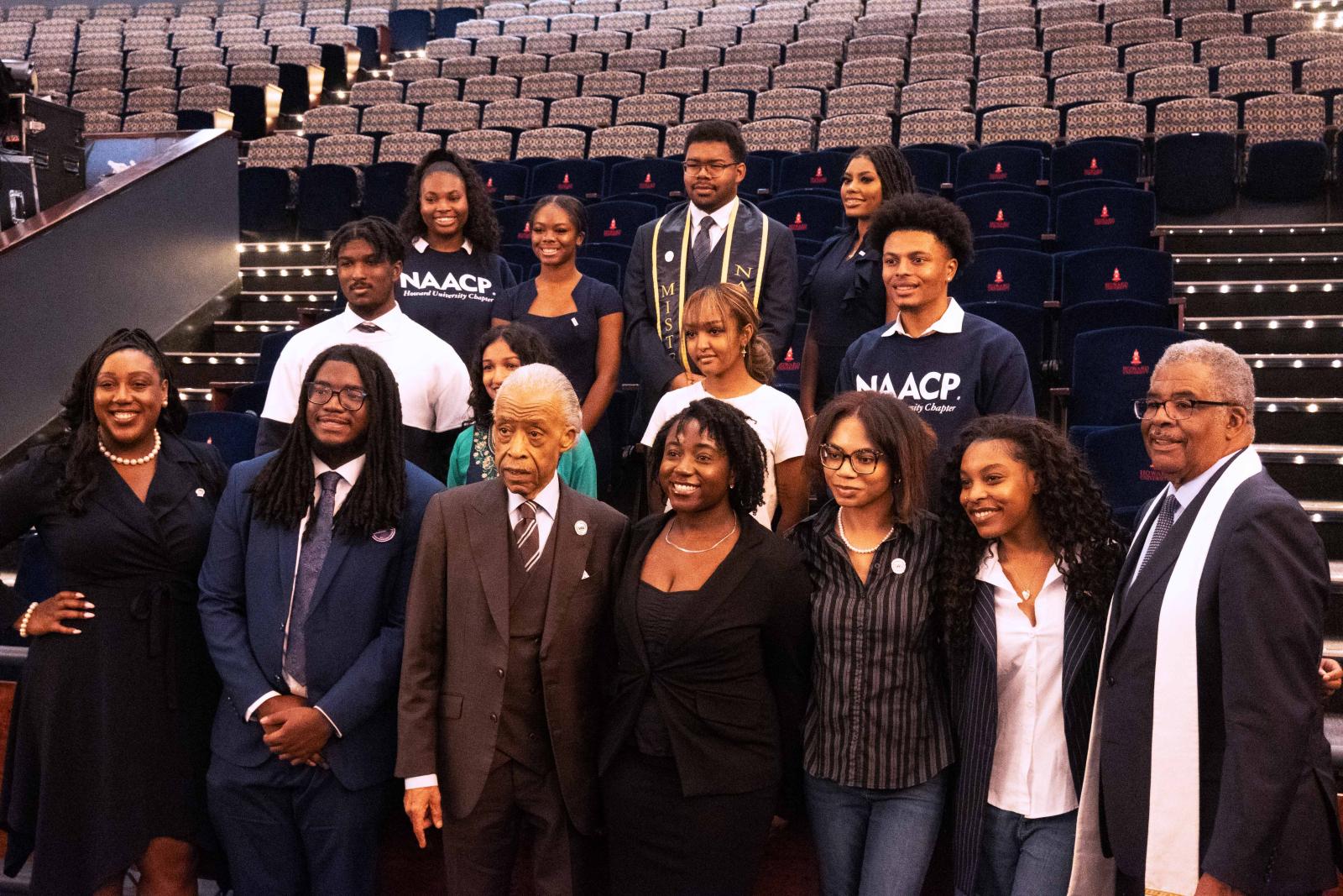 A group of 15 people posing for an image. The people are spaced out into three rows. Some of the people are wearing sweatshirts that say NAACP.