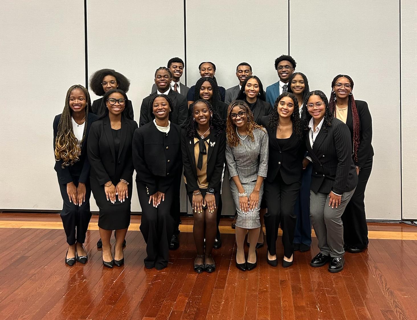 A group of 17 college students smiling for the camera. They are all wearing suits. The students in the front row have their hands in their laps