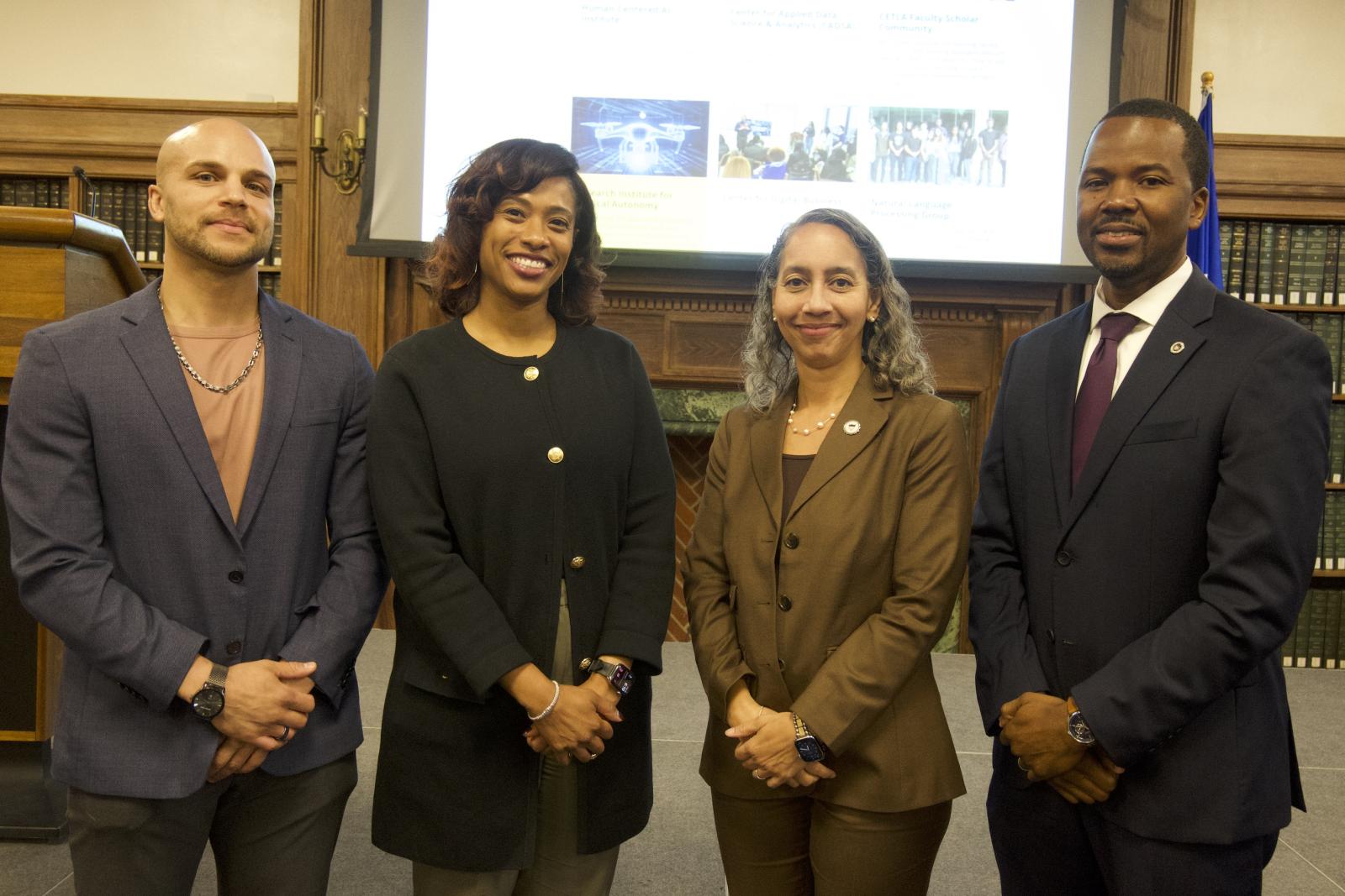 Four people standing with their hands crossed. They are smiling at the camera